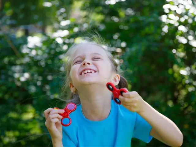 smiling kid girl holding two fidget spinner toy